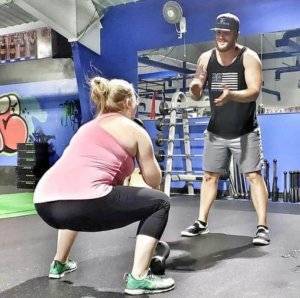 A woman squats in preparation to throw a medicine ball to her trainer.